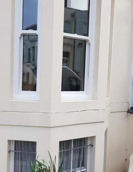 White bay windows with a plant pot in front, located on the corner of a building.